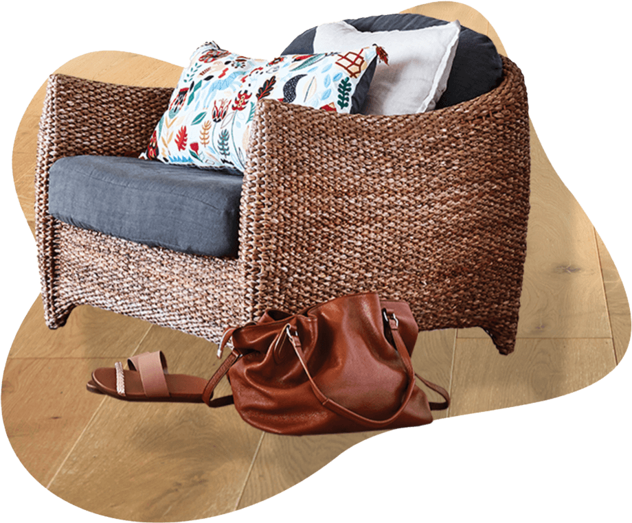 A wicker armchair with a grey cushion and colorful pillows sits on a wooden floor. Nearby, a brown leather bag and a single sandal rest beside the chair. This cozy scene subtly reflects the inviting ambiance that Spark Interact's web design and branding service aims to create for your online presence.